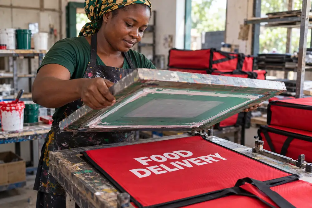 Screen printing a white food delivery design on a red bag fabric panel before assembly
